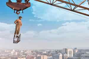 Free photo ready for the day. low angle portrait of a young muscular retro builder posing on a crossbar hanging from a crane on a skyscraper