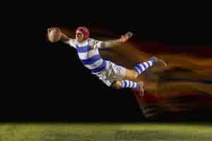 Free photo ready to fly for win. one caucasian man playing rugby on the stadium in mixed light