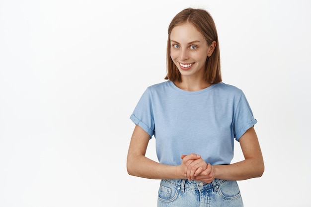 Free Photo ready to help you. smiling young blond woman, girl assistant, look friendly, holding hands together near chest as if consulting, helping customer, white background