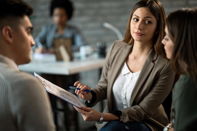 Real estate agent showing the terms of a contract to young couple while analyzing paperwork on a meeting