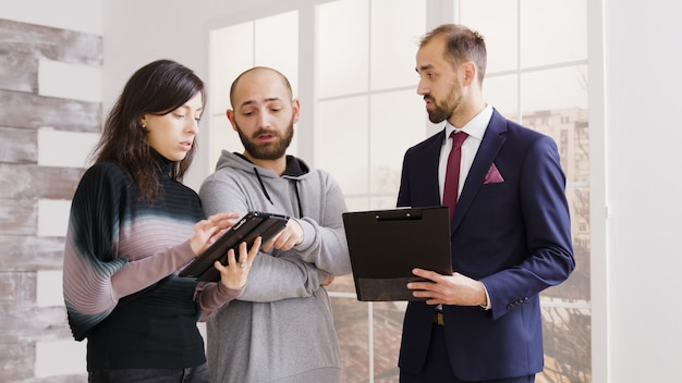 Real estate agent talking with couple and holding documents homeowning contract in new apartment.