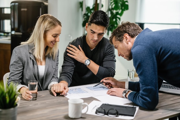 Real estate agent and young couple going through their housing plan on a meeting