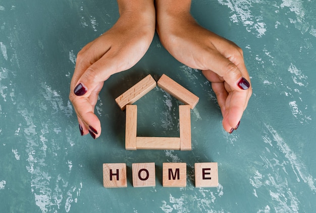 Real estate concept with wooden blocks flat lay. hands enclosing house model.