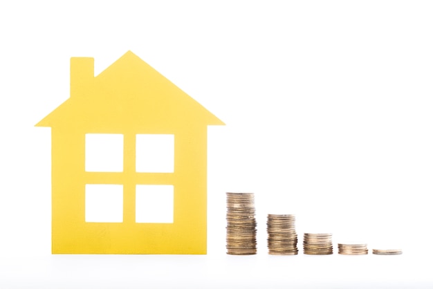 Real estate house and piles of coins on white background