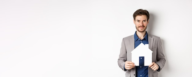 Free Photo real estate and insurance concept salesman in grey suit showing paper house cutout selling property