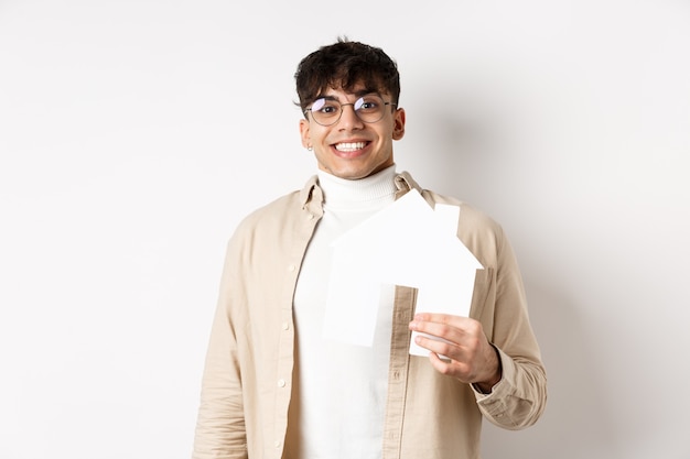 Real estate and mortgage concept cheerful young guy renting apartment showing paper house cutout and...