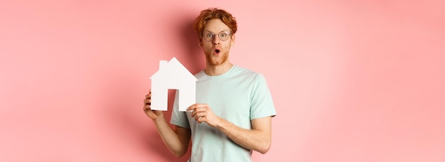 Free photo real estate surprised young man with red hair and beard wearing glasses and tshirt showing paper hou