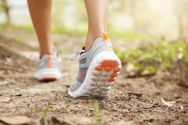 Rear cropped shot of athletic legs of woman jogger wearing pink running shoes during jogging exercise outdoors.