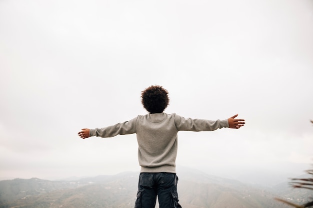 Rear view of an african young man standing on top of mountain outstretching his hand