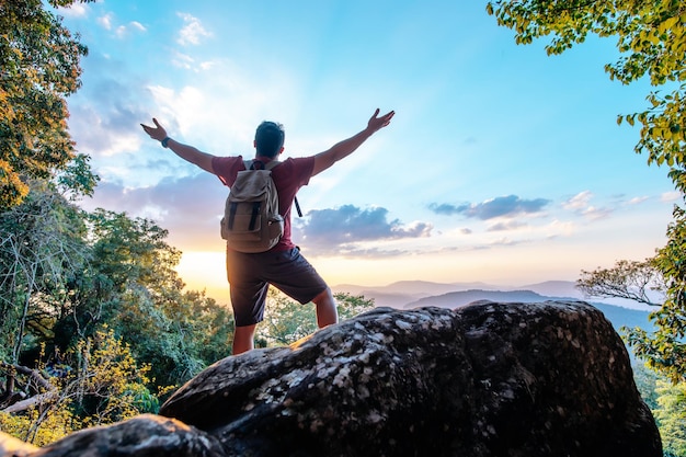 Free photo rear view back of young asian hiking man standing and riseup hands with happy on peak of rocky mountain copy space