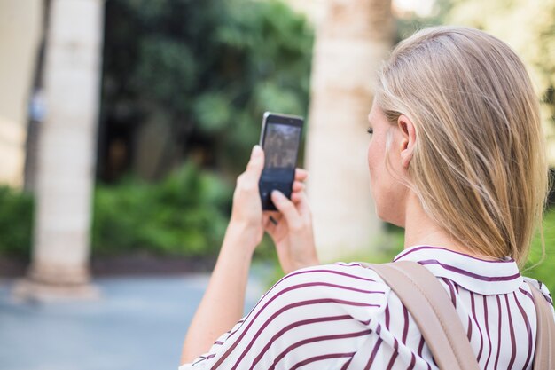 Rear view of blonde young woman taking photograph on mobile phone