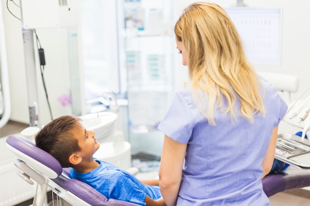 Rear view of a dentist standing in front of boy sitting on dental chair