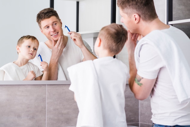 Rear view of a father and son looking in the mirror holding razor in hand