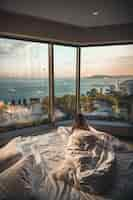 Free photo rear view of a female lying on bed looking at the beach through the glass windows