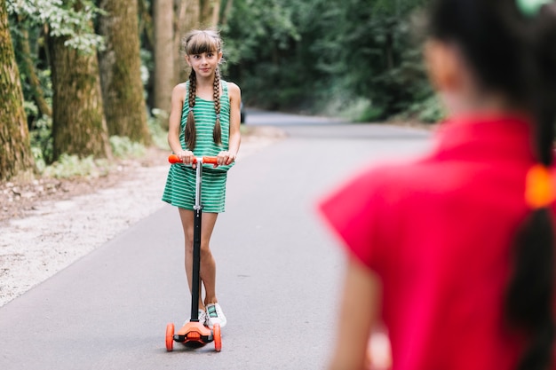 Free Photo rear view of girl looking at her friend standing on push scooter