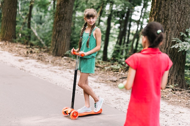 Free photo rear view of a girl looking at her friend standing on push scooter