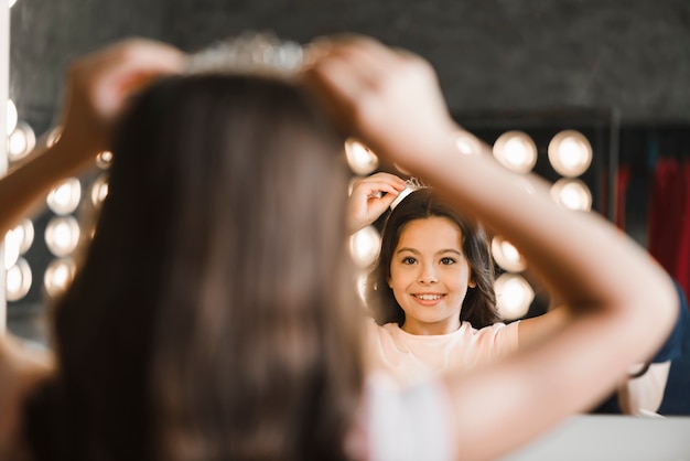 Rear view of girl wearing crown on his head looking in the mirror