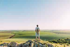 Free photo rear view of male hiker with backpack looking at green rolling landscape