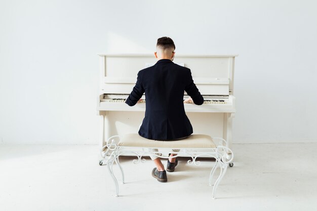 Rear view of a man playing the piano sitting against white wall