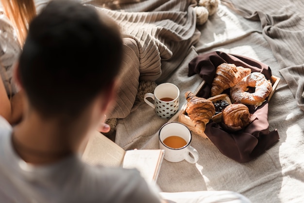 Free Photo rear view of a man reading book with breakfast on bed