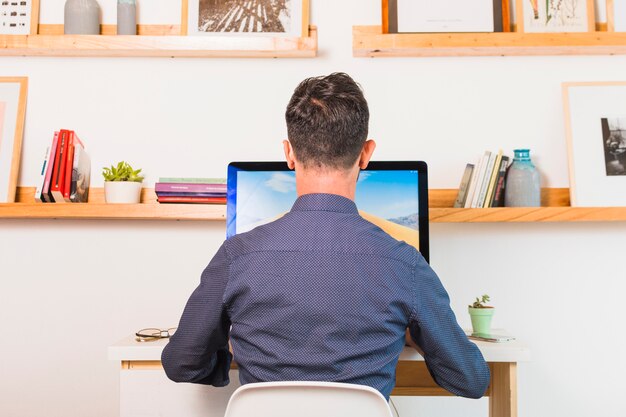 Rear view of man sitting on chair using computer in office