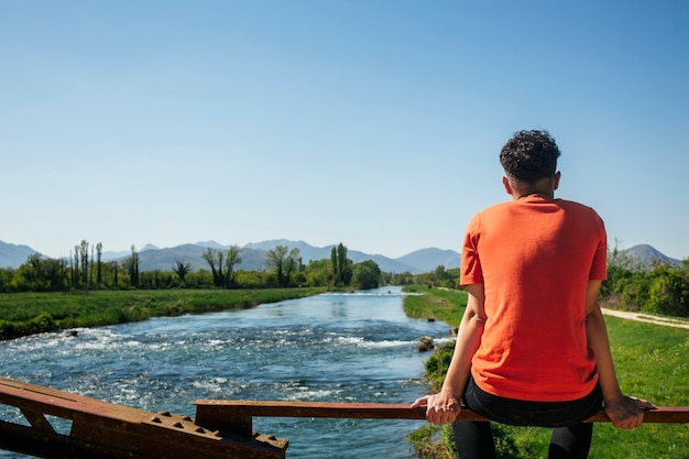 Rear view of man sitting on railing near idyllic river