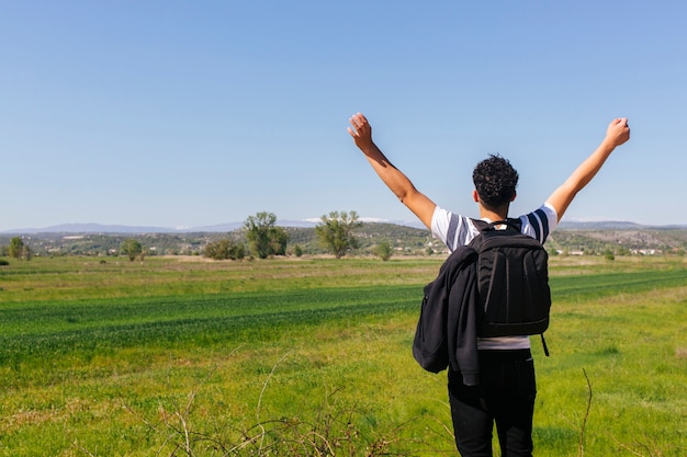 Rear view of man standing near beautiful green landscape with backpack