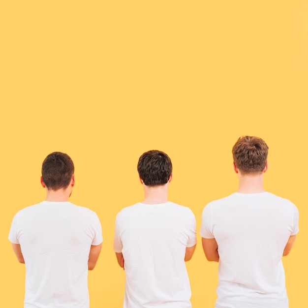 Free photo rear view of a men in white t-shirt standing against yellow background