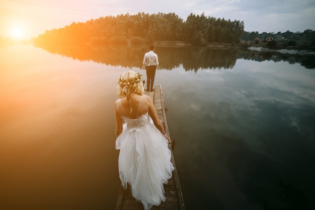 Free photo rear view of newlyweds on a wooden walkway at sunset