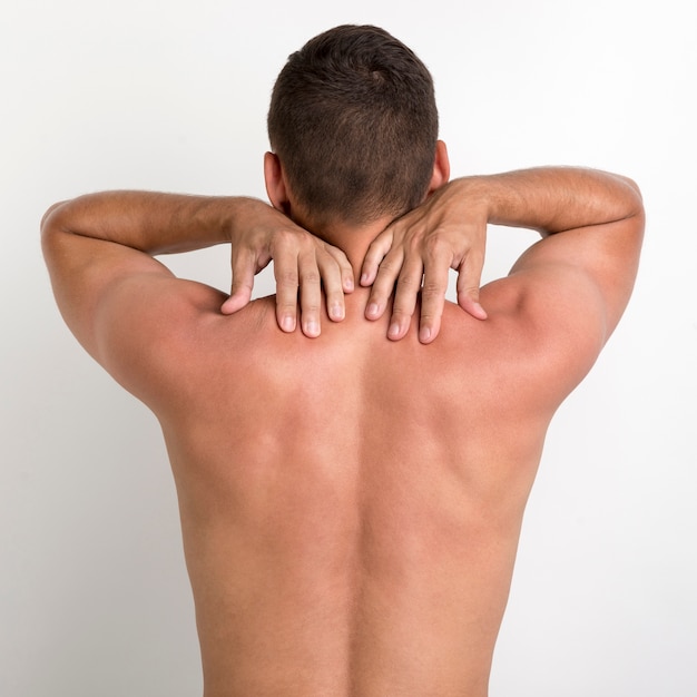 Rear view of shirtless man having back pain standing against white wall