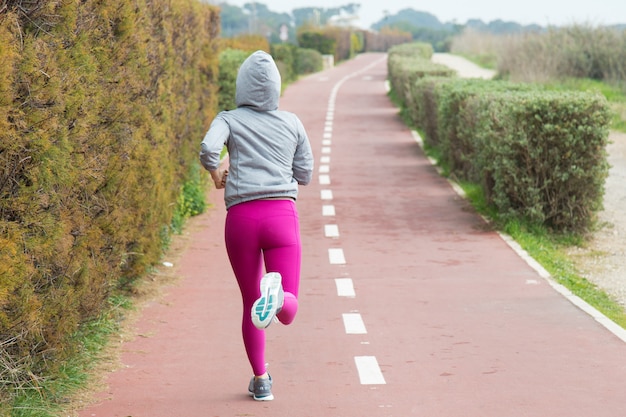 Free photo rear view of sporty woman in pink leggings running over track