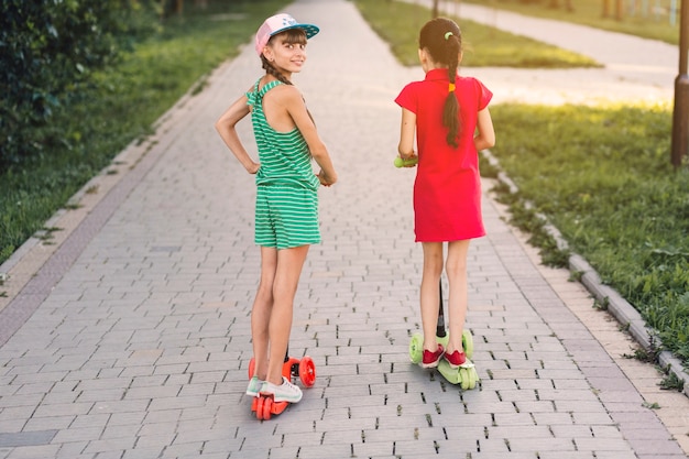 Free photo rear view of two girls riding push scooter in the park