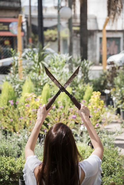 Free photo rear view of a woman holding gardening scissors in front of plants growing in greenhouse