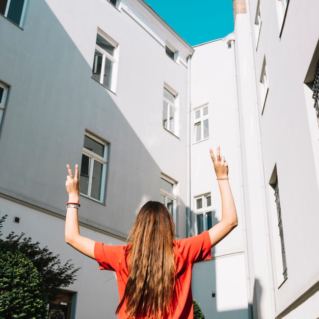 Free photo rear view of a woman making peace gesture near building