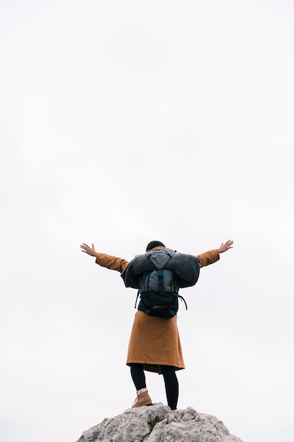 Rear view of a woman standing on the top of mountain raising her arms against sky