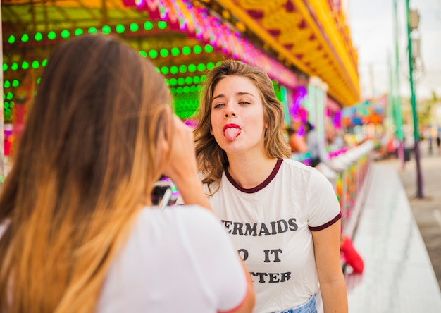 Rear view of woman taking photo of her friend showing tongue at amusement park