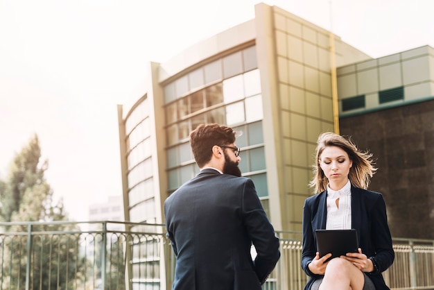 Rear view of young businessman looking at businesswoman using digital tablet at outdoors