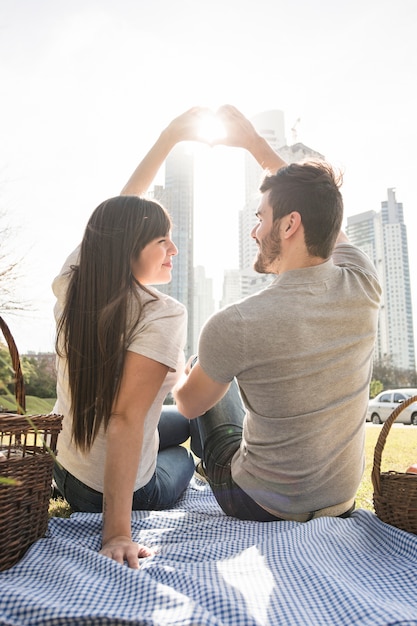 Free Photo rear view of young couple making heart shape with hand in sunlight at picnic