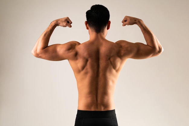 Free photo rear view of a young man flexing his muscles and showing his muscular back