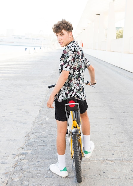 Rear view of a young man with bicycle looking at camera