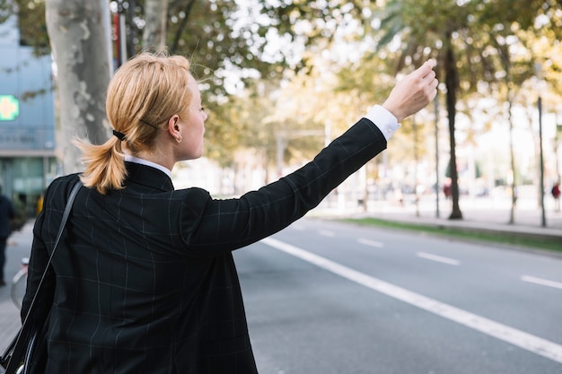 Free photo rear view of a young woman hailing rideshare taxi car on road