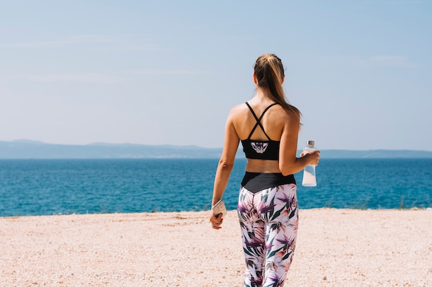 Free Photo rear view of a young woman holding water bottle overlooking the sea