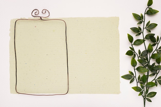 Free photo rectangular empty frame on paper near the artificial green leaves on white backdrop