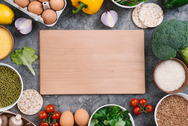 Rectangular wooden chopping board surrounded with healthy vegetables