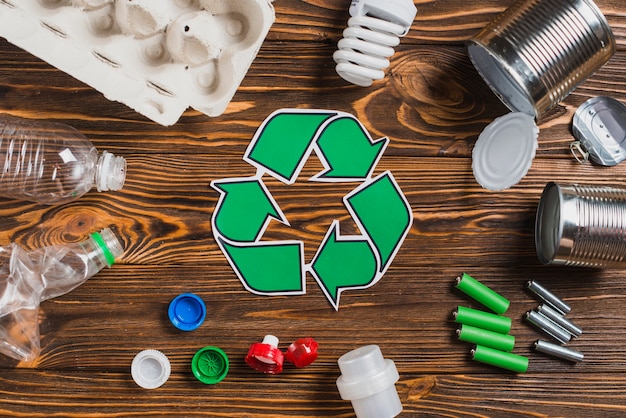 Recycle symbol surrounded with waste items on brown wooden textured background