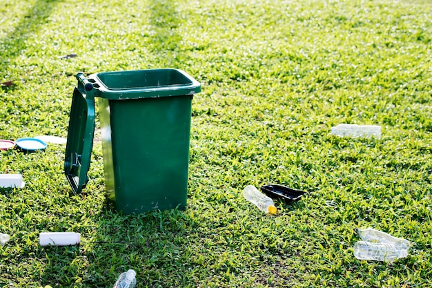 Recycling campaign with green bin and wasted plastic bottles on the field