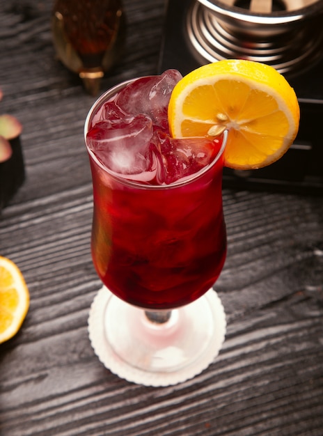 Red alcohol cocktail in glass with ice cubes and lemon slice