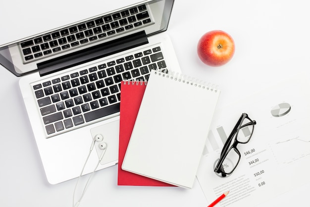 Free photo red apple,earphones,laptop,spiral notepad and eyeglasses on budget plan over white background