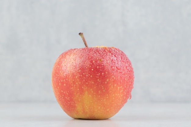 Red apple with water drops on stone table.