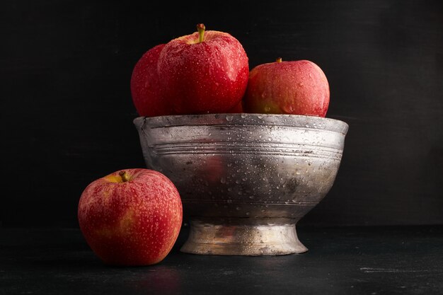 Red apples in a metallic cup on black surface. 